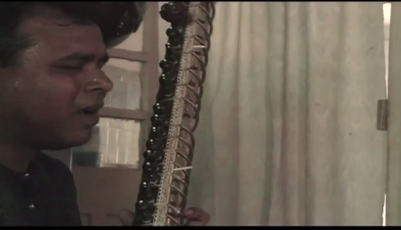 A musician plays the sitar in a curtained room.